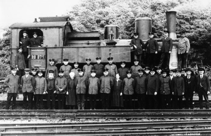 Vor und in einer Dampflok stehen die Eisenbahner und zwei Frauen zum Gruppenfoto. Ebernburg, um 1920