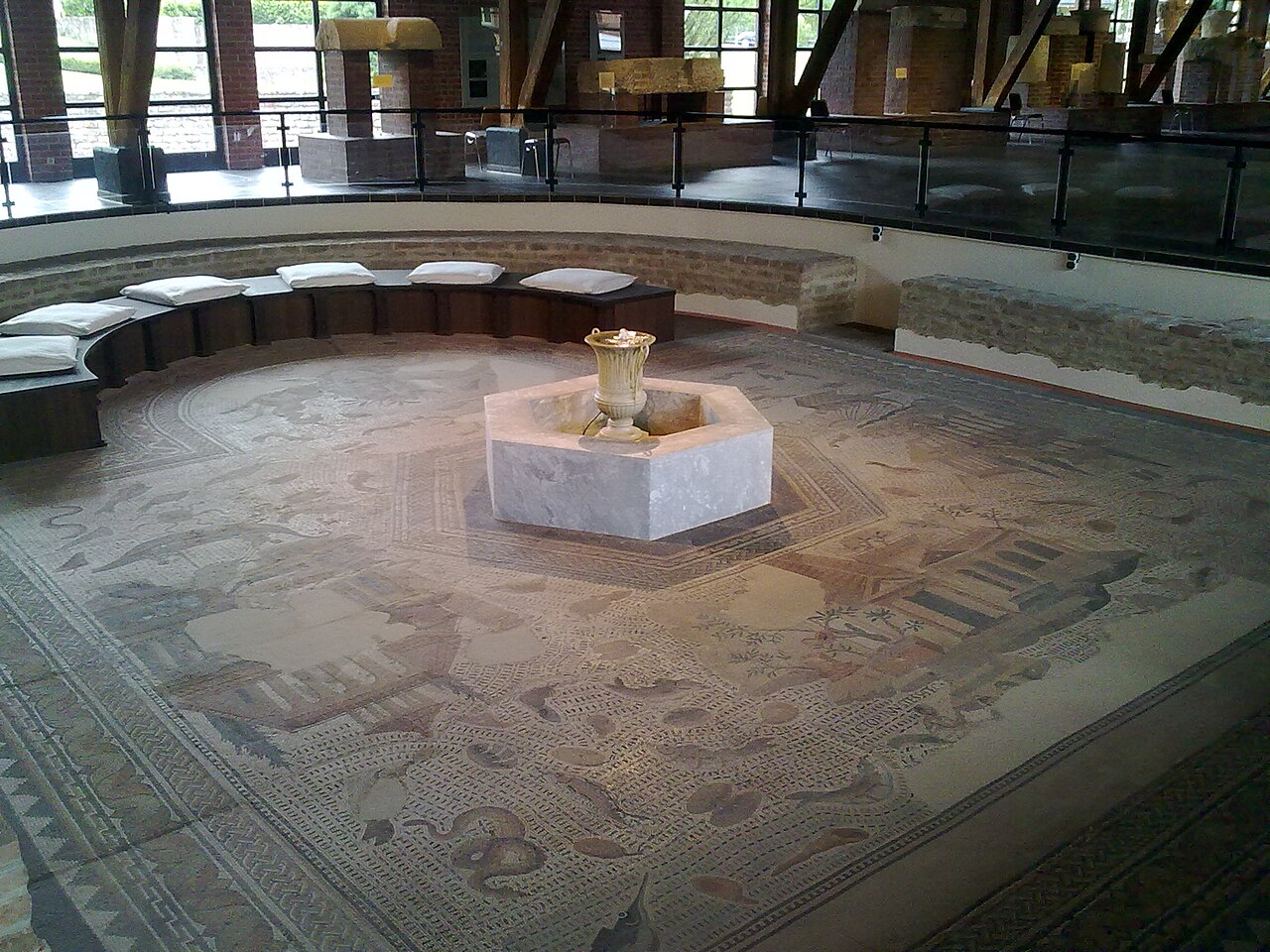 Blick auf das Oceanusmosaik, In der halbrunden Apsis steht das Sitzpodest mit Kissen für sechs Personen. Im Zentrum des Mosaiks steht eine Brunnenfassung; in ihr sprudelt Wasser aus einem marmornen Kelchkrater (Gefäß in Form einer um 90 Grad gedrehten Akanthus-Blüte).
